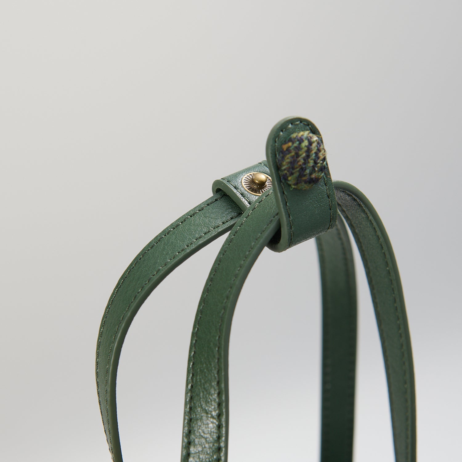 Close-up of tan leather handle and hardware on green herringbone bucket bag