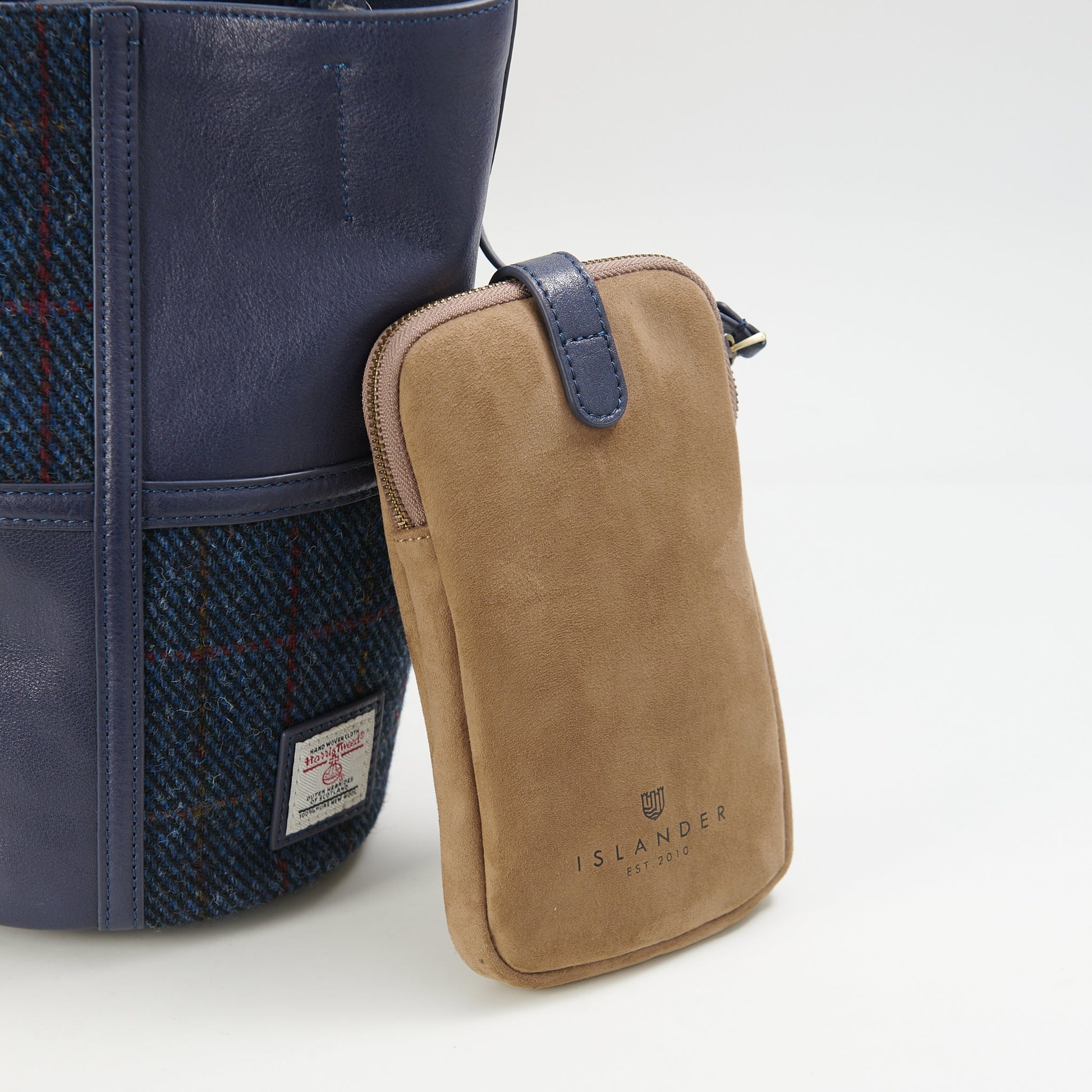 Islander tan suede phone pouch with navy strap beside bucket bag