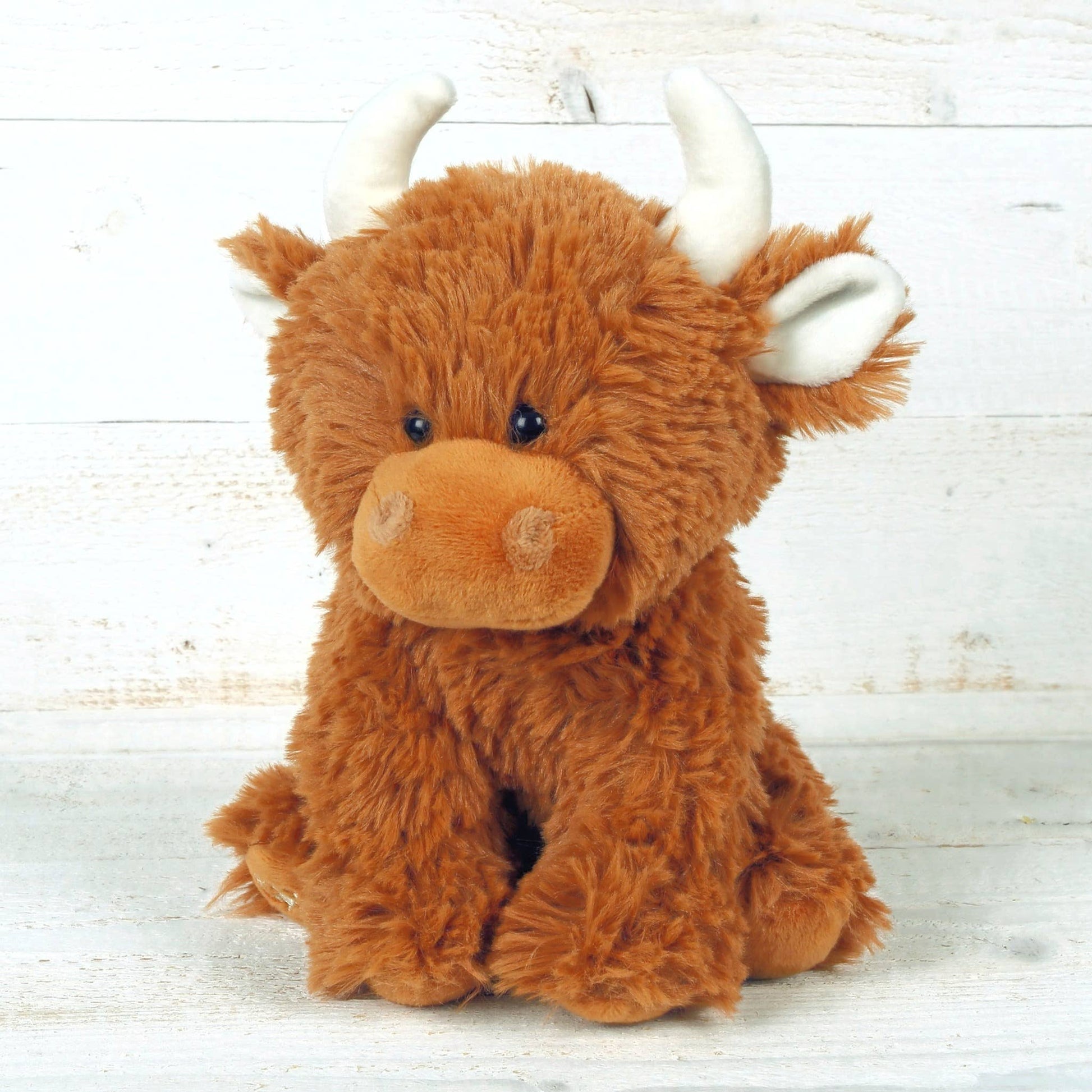 Highland cow soft toy with cream horns photographed on whitewashed wooden boards