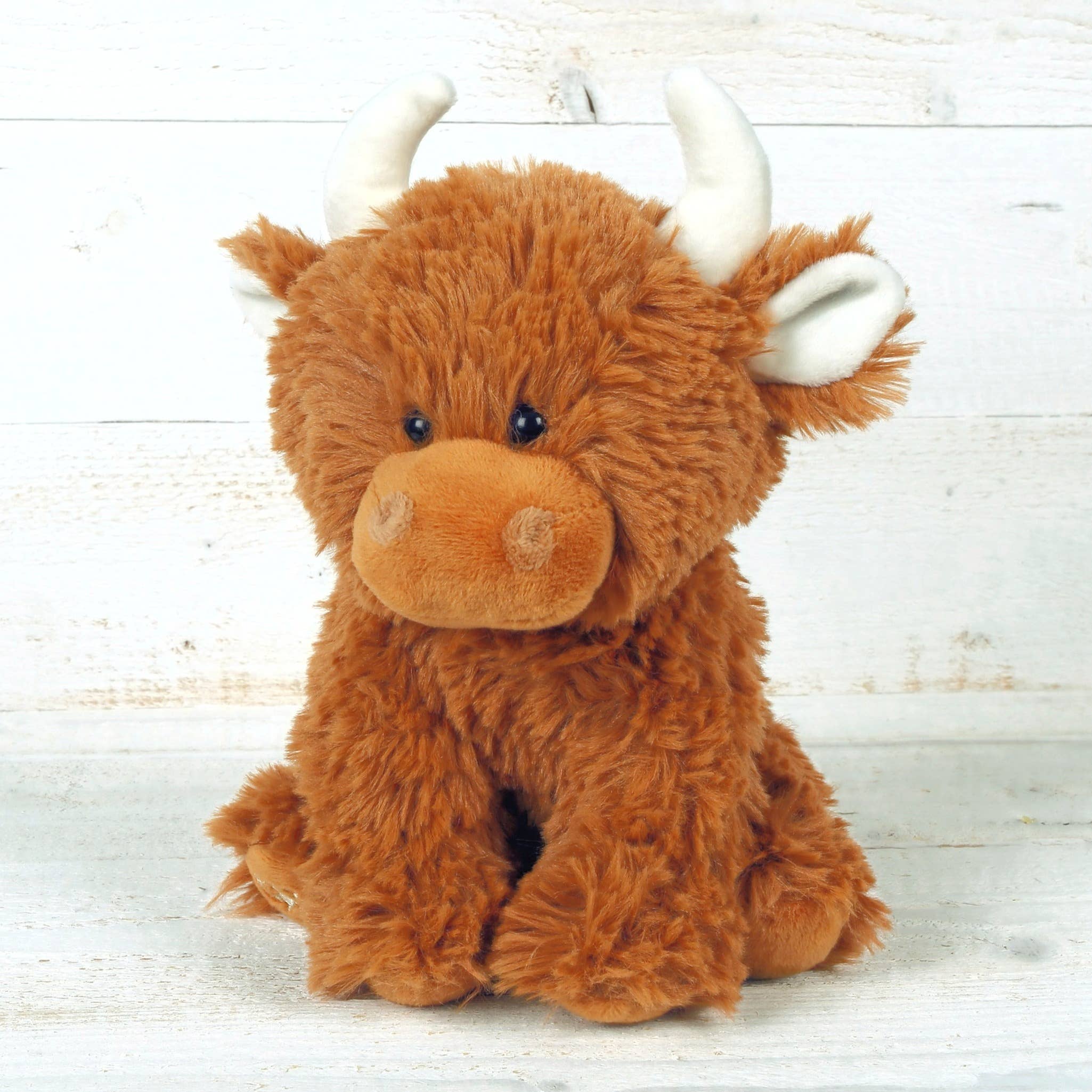 Highland cow soft toy with cream horns photographed on whitewashed wooden boards