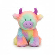 A plush highland cow toy with fluffy pastel rainbow fur in pink, orange, yellow, green, blue, and purple, sitting against a neutral beige fabric background.