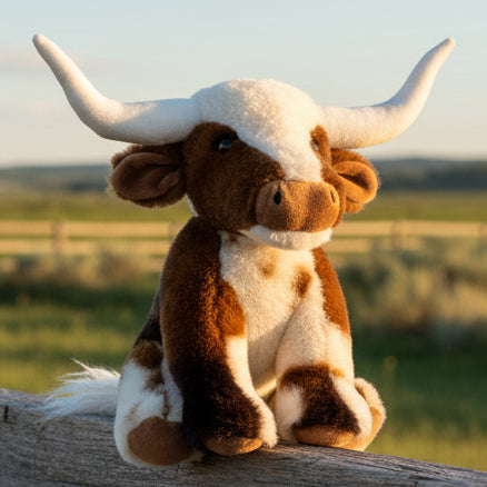 Texas Longhorn cow soft toy on wooden fence with countryside background