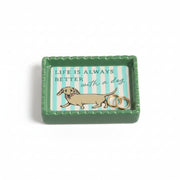 Ceramic trinket dish with dachshund design and striped background holding gold earrings.