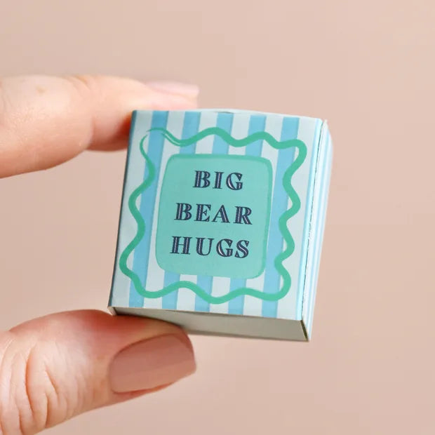 Closed blue striped matchbox held in fingers showing bear hugs message