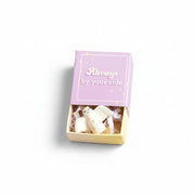 Ceramic angel nestled inside open lilac matchbox on cream background