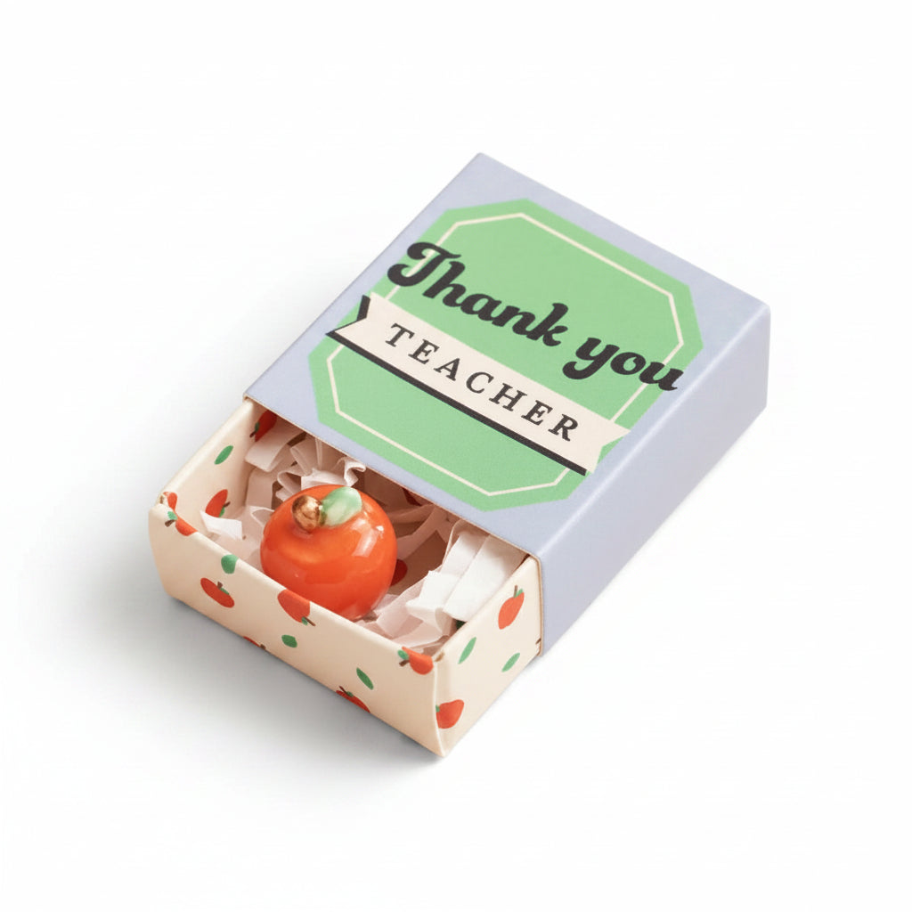 Ceramic apple inside open matchbox with blue and green lid on cream background