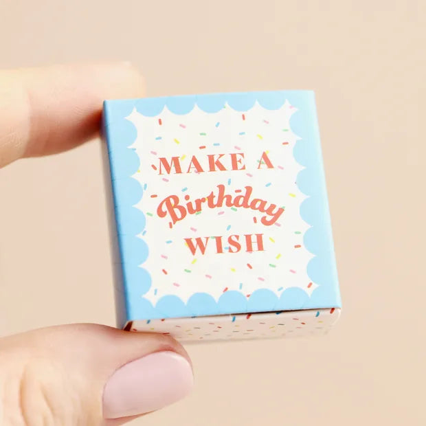 Hand holding closed blue matchbox with confetti and sprinkle design on cream background