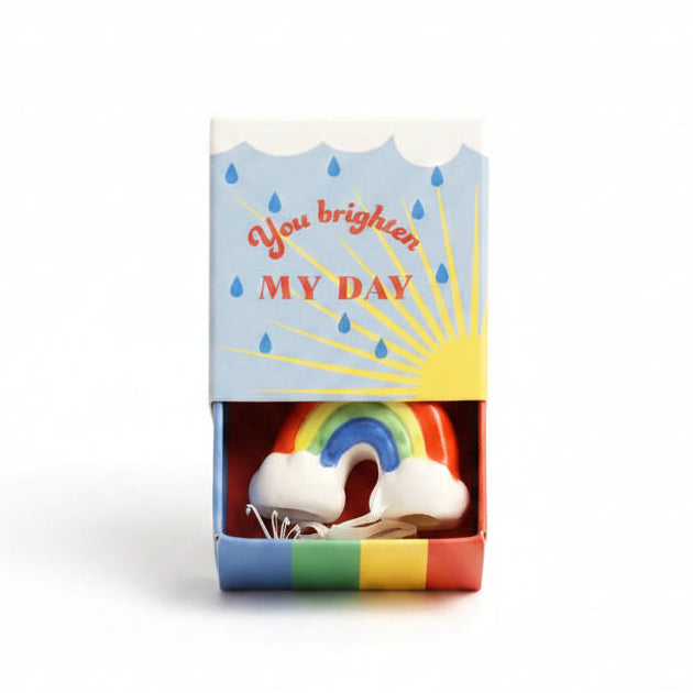 Ceramic rainbow inside open blue matchbox with sunshine and raindrop design on cream background