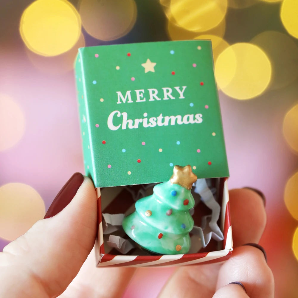 Christmas tree matchbox token held against warm festive bokeh lights