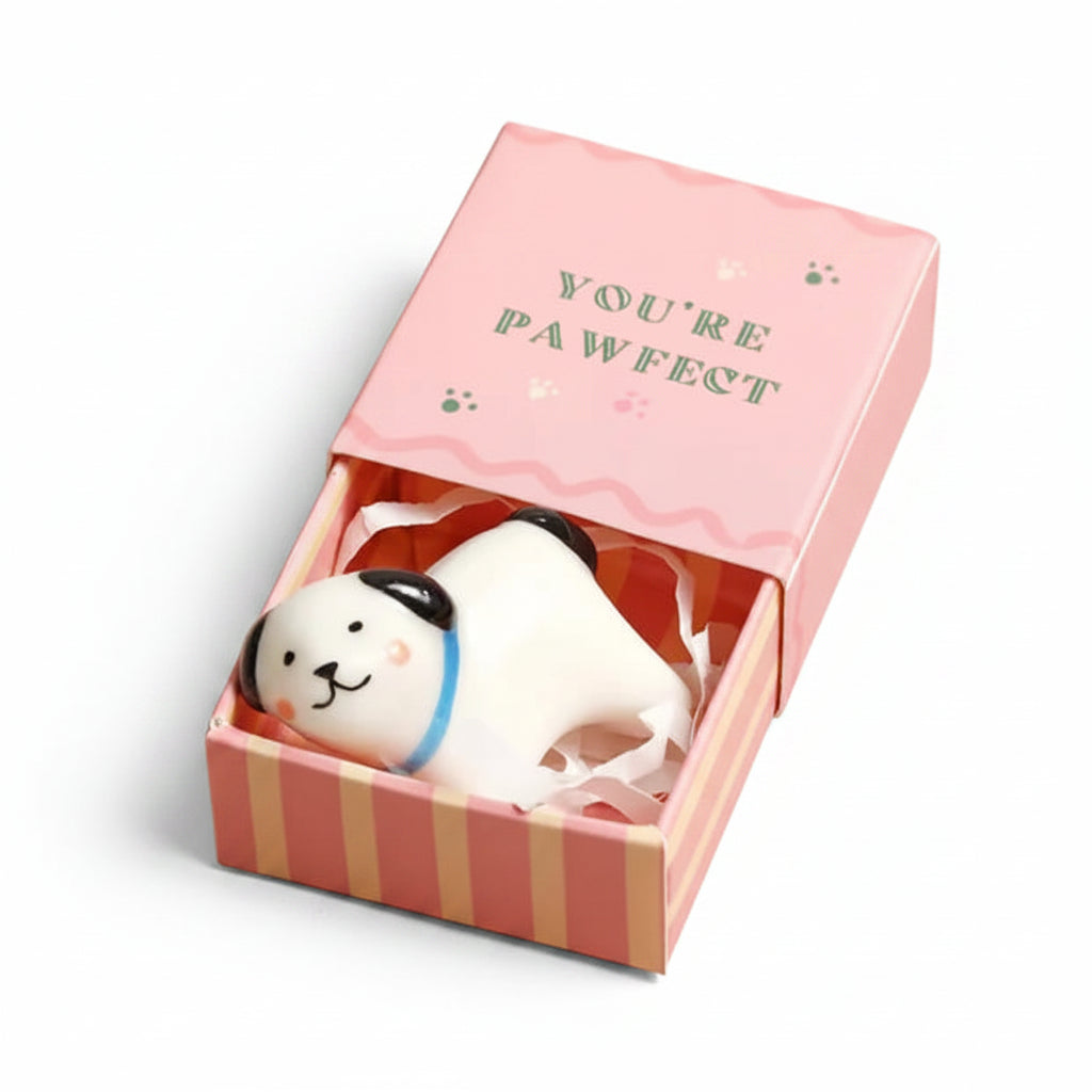 White ceramic dog token in open pink matchbox on beige surface