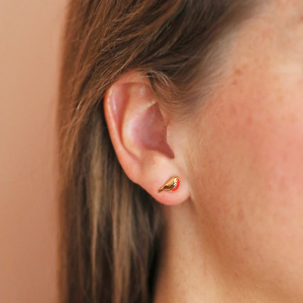 Gold enamel robin stud earring worn in an ear lobe, close up