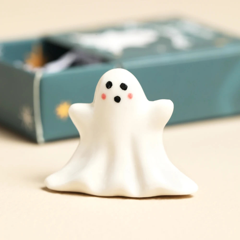 Glossy white ceramic ghost token with rosy cheeks beside its matchbox