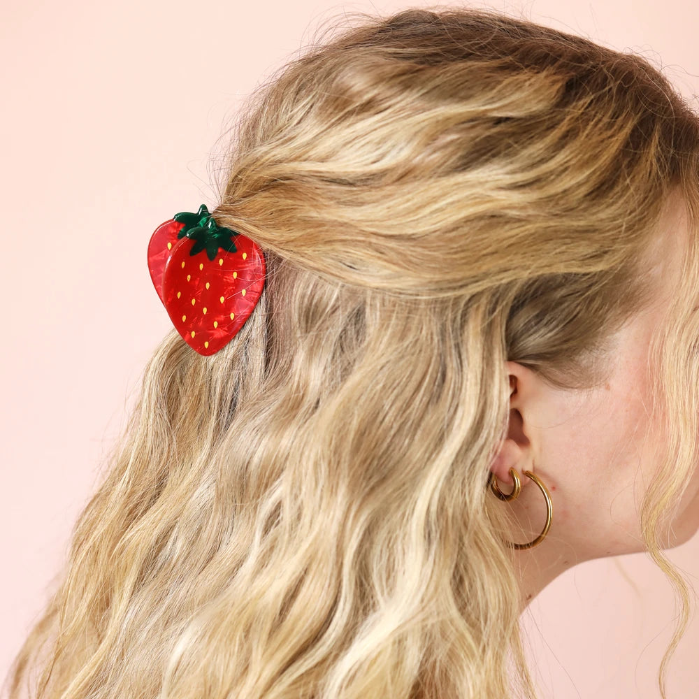 Strawberry claw clip worn in blonde hair in a half-up style
