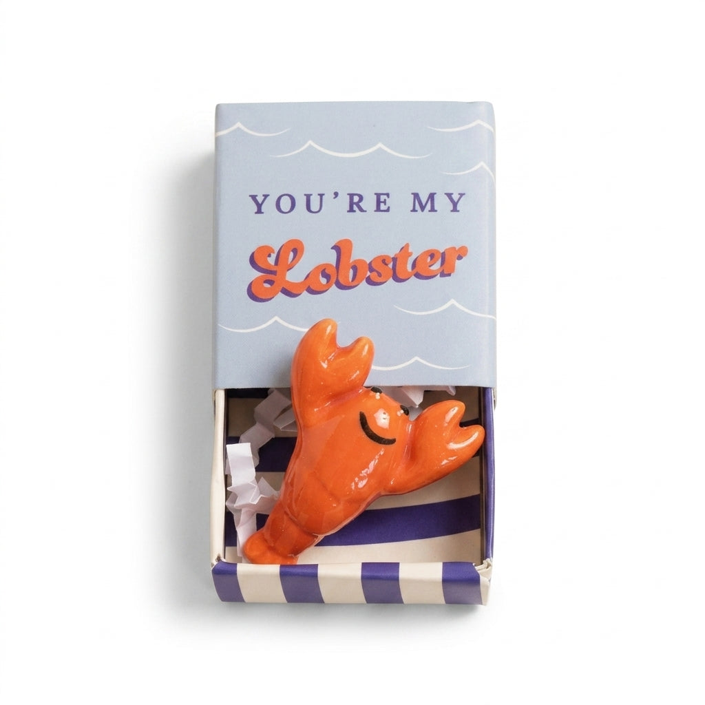 Tiny ceramic lobster token in its matchbox on white