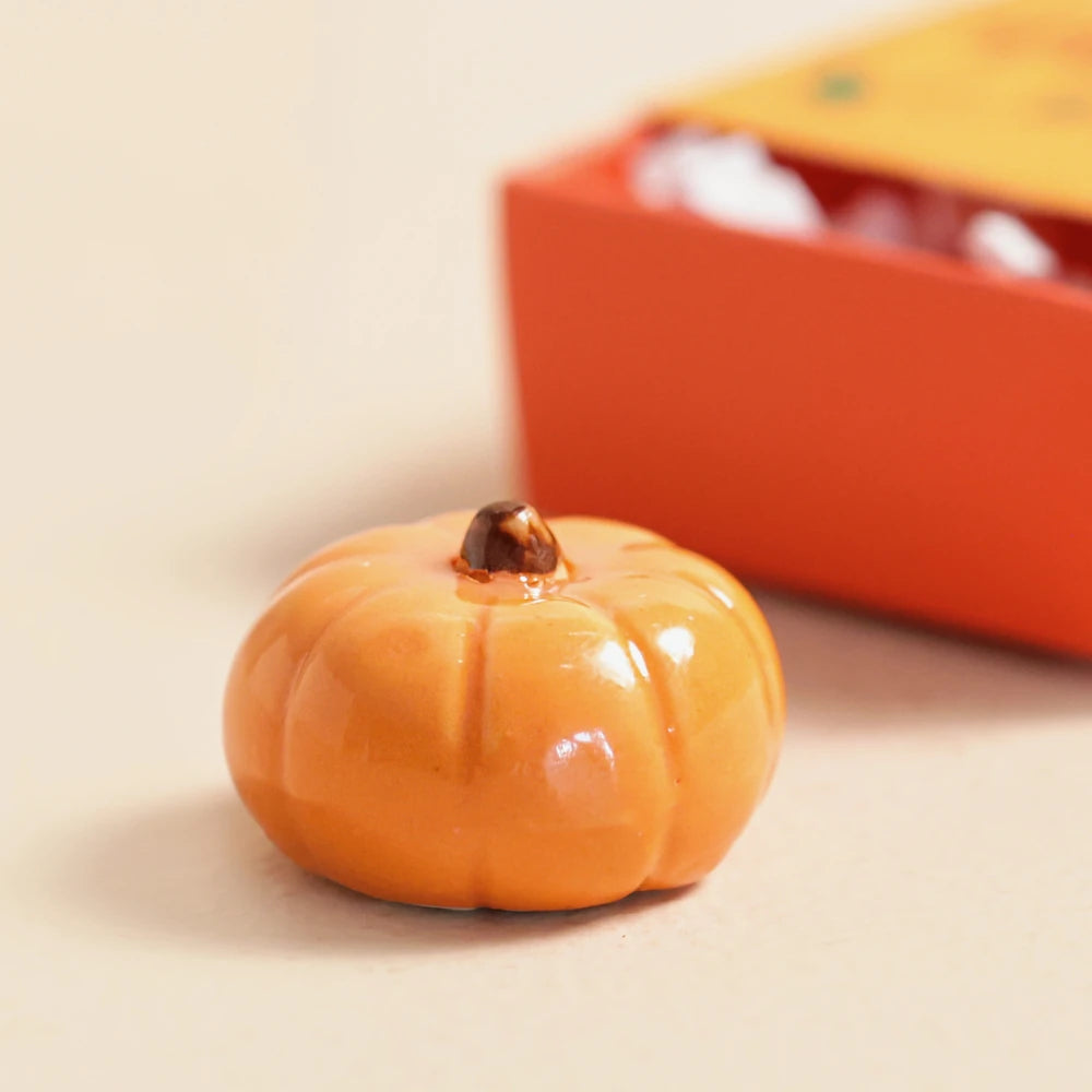 Glazed orange ceramic pumpkin token beside its open matchbox