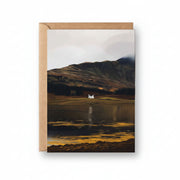 Illustrated Loch Eil greeting card featuring a white cottage by calm water with dramatic Scottish hills in the background.