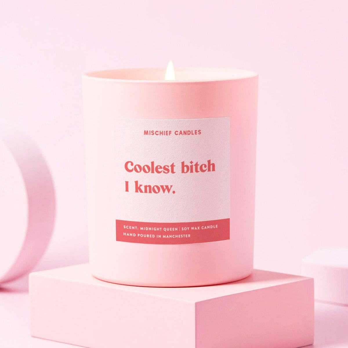Coolest Bitch I Know funny candle in a pink glass jar, lit on a pink stand