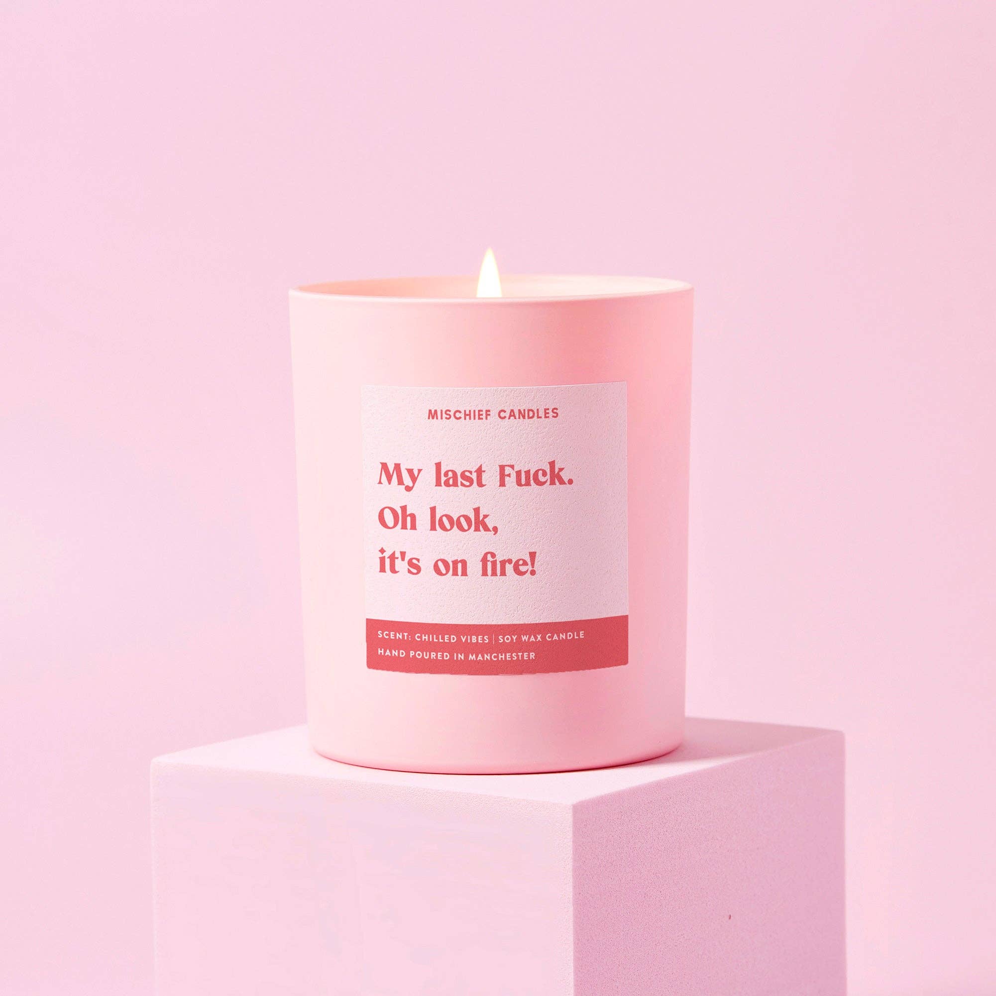 My Last Fuck candle in a matte pink jar, lit against a pale pink backdrop
