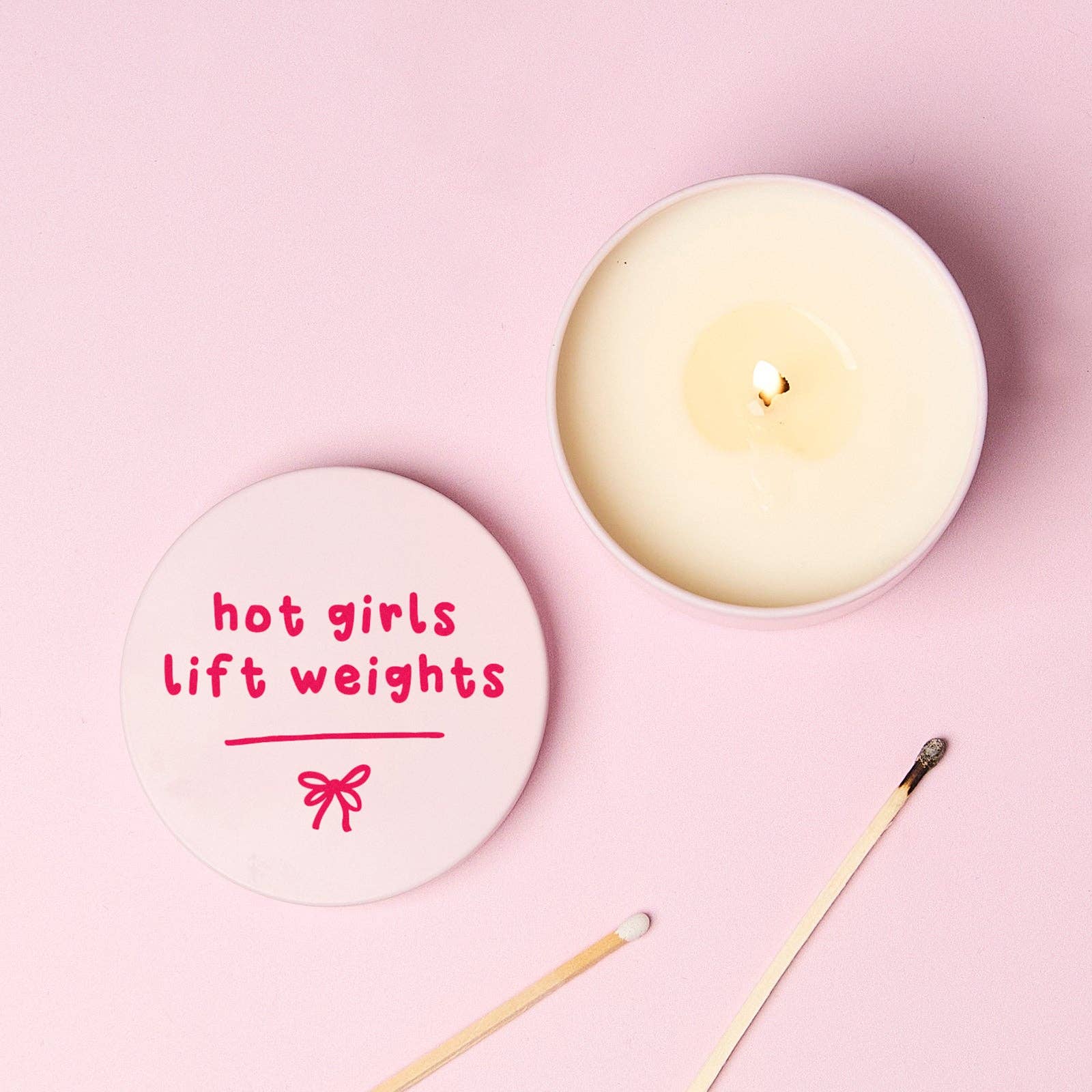 Hot Girls Lift Weights candle lid beside lit tin from above on pink