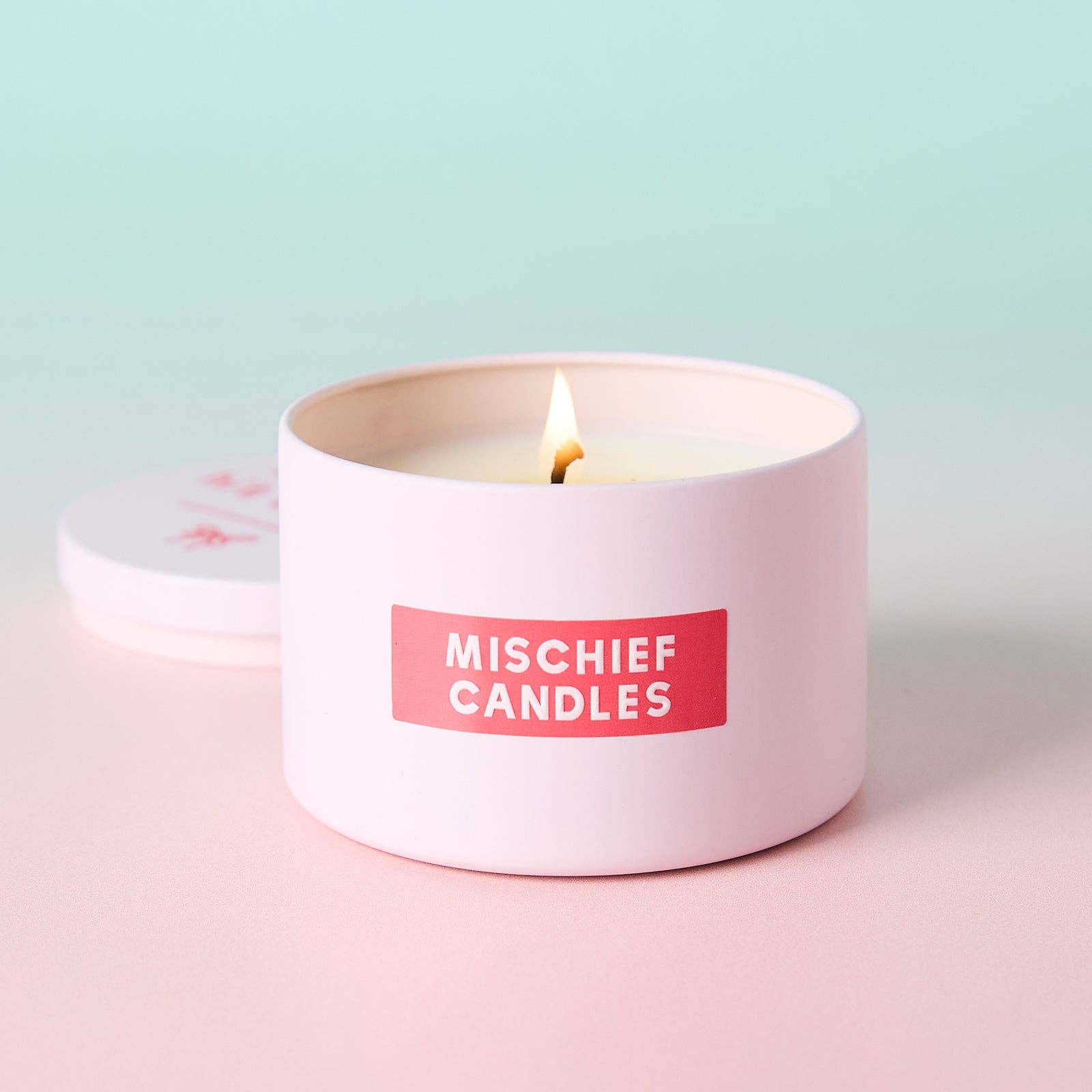 Lit pink tin candle with lid behind on pink and mint backdrop