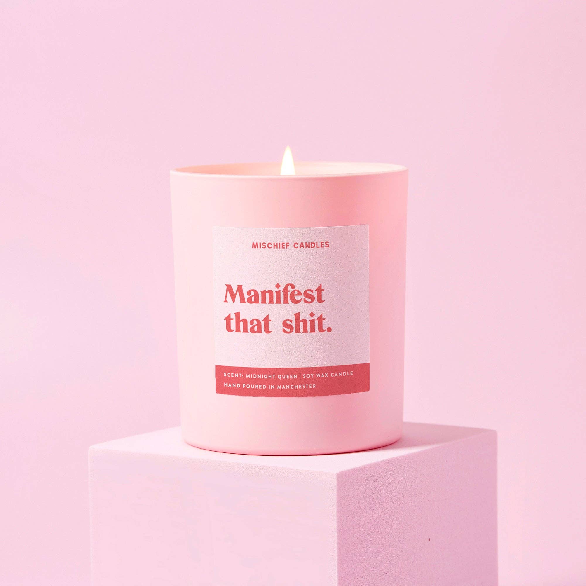 Manifest That Shit positivity candle in matte pink jar lit on a pink backdrop