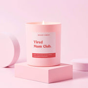 Tired Mum Club pink container candle burning on pale pink display block