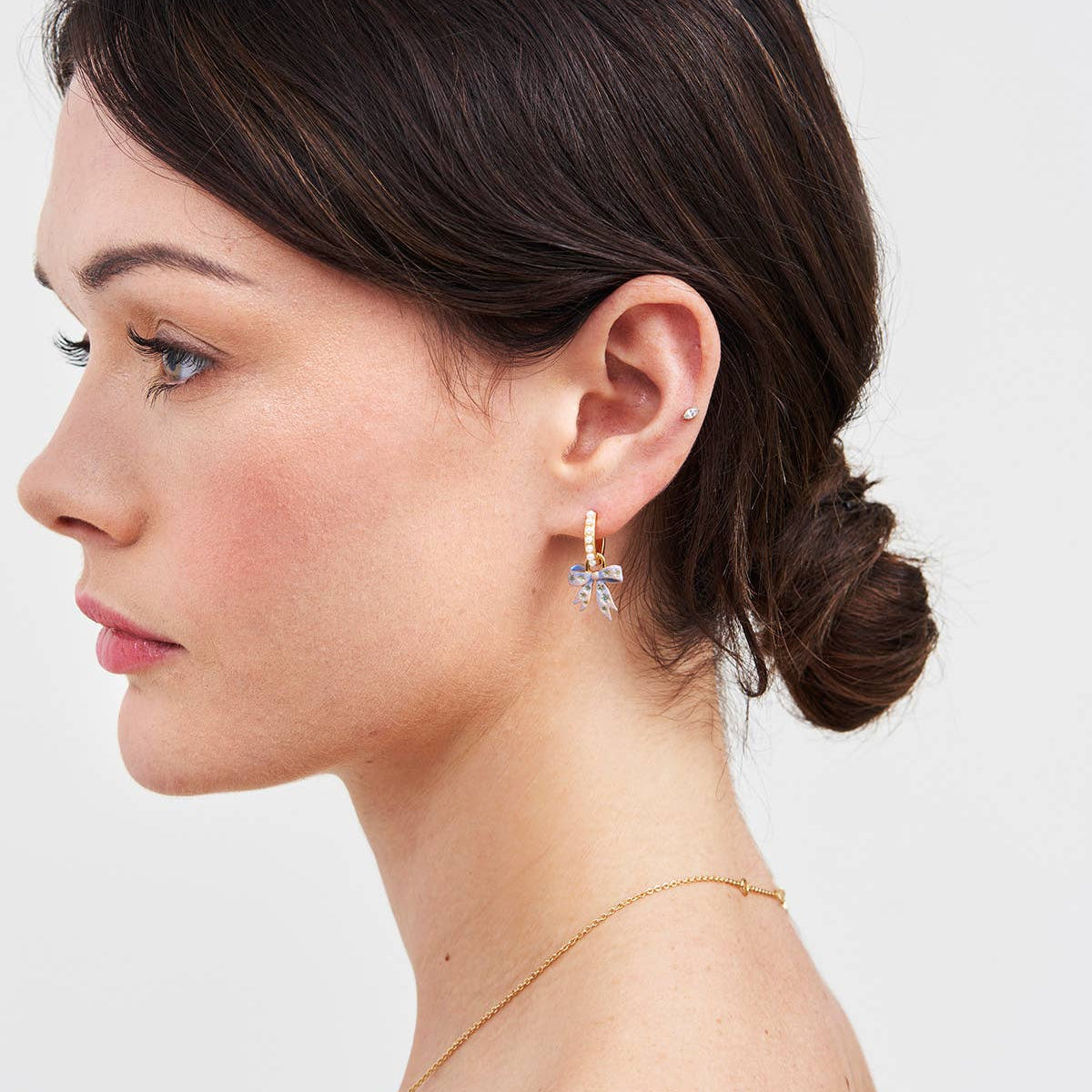 Side profile of a model wearing a gold huggie earring with pearl detail and bow charm.