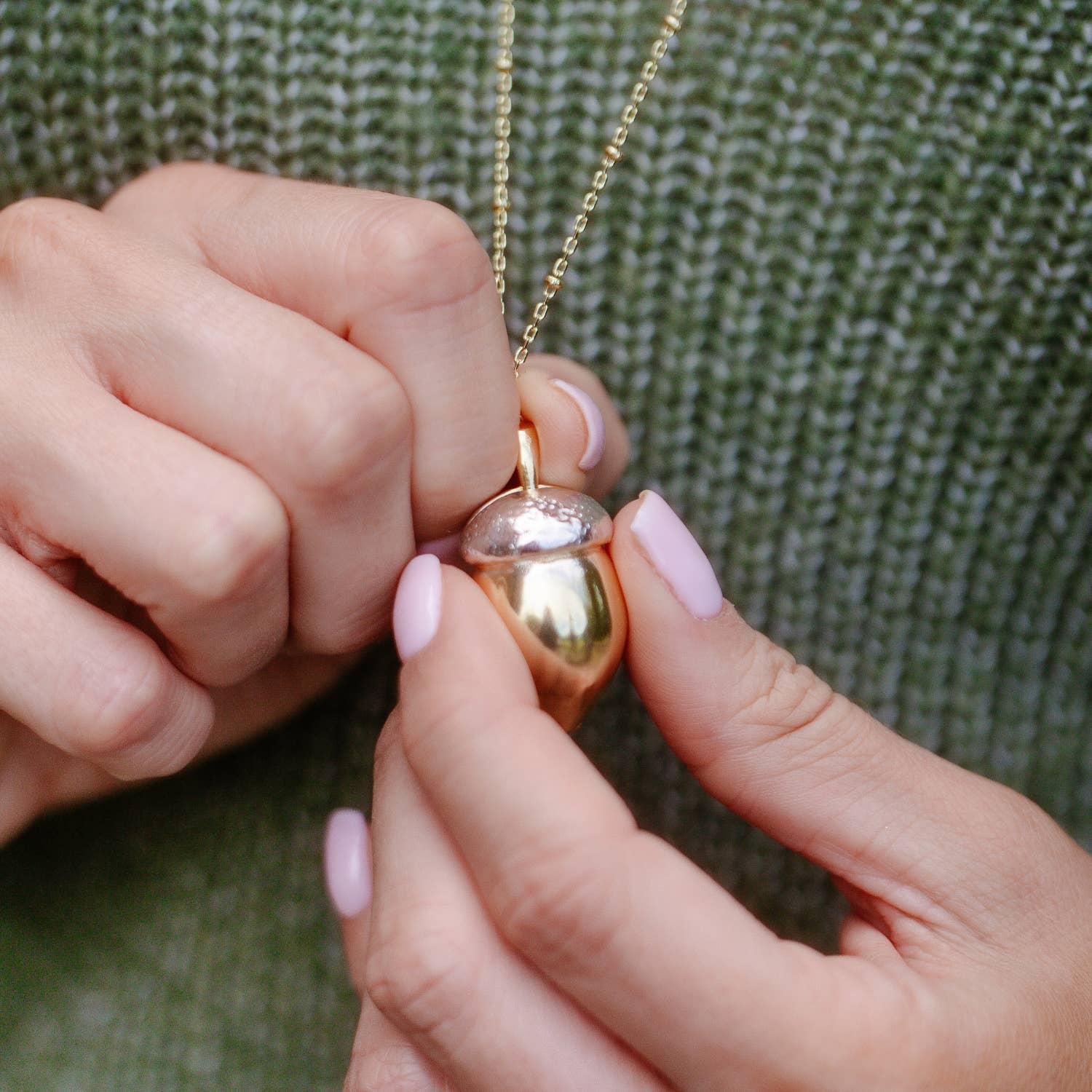 Hands holding closed Squirrel Acorn Locket showing shiny gold and silver two-tone finish.