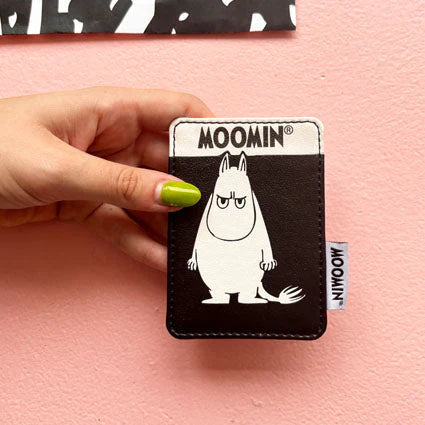 Hand holding Moomin Angry Moomin Cardholder in black and white PVC with bold Moomin character design, against a pink background.
