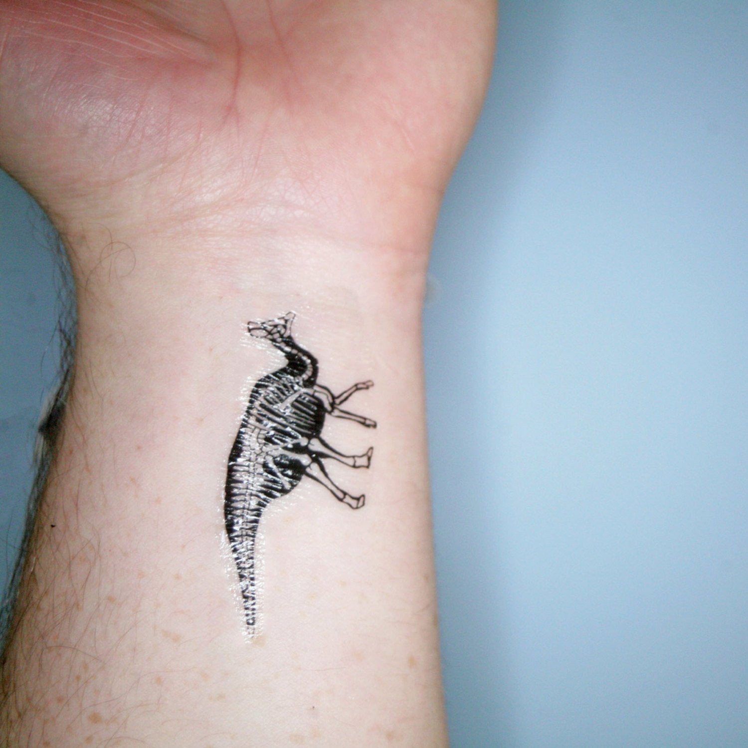 A dinosaur transfer tattoo applied to a wrist