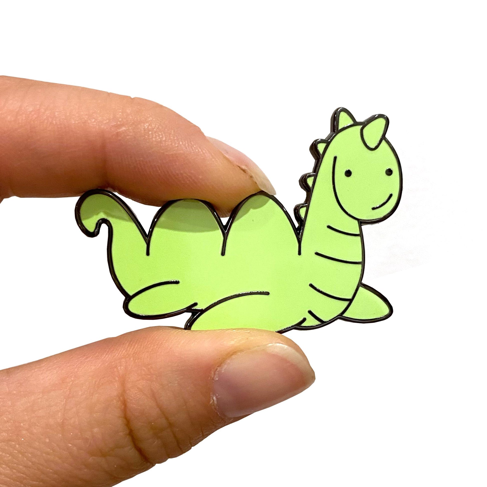 Green Loch Ness Monster enamel pin held between finger and thumb