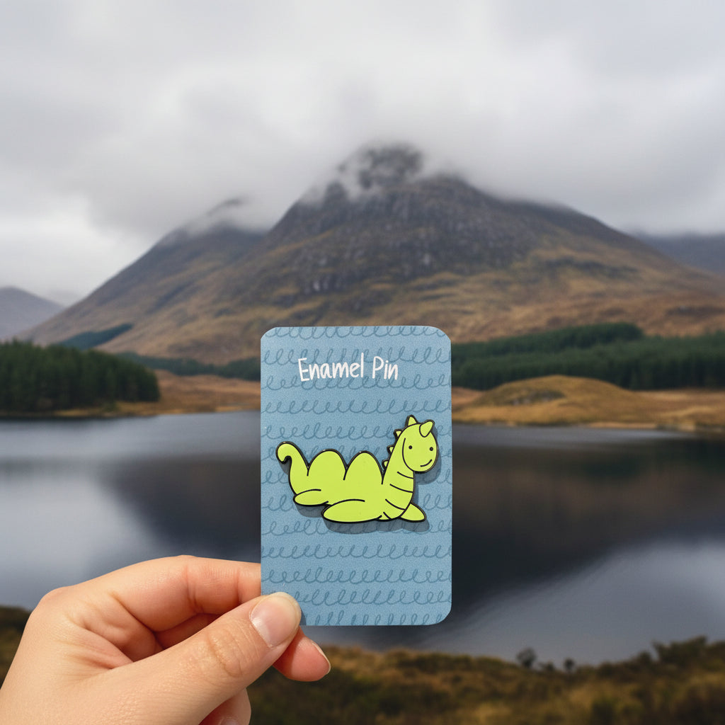Nessie enamel pin on its illustrated backing card, held in a hand
