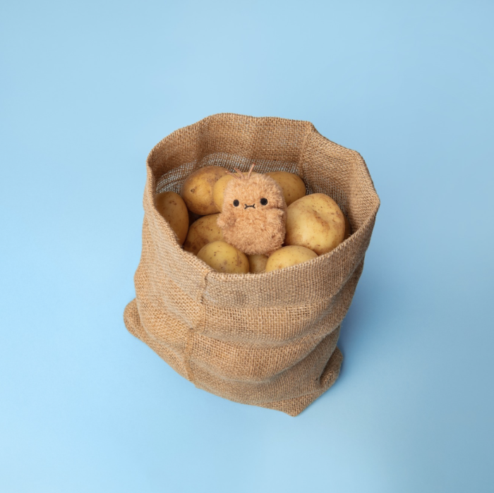 Ricespud potato plush keyring peeking from a hessian sack of real potatoes