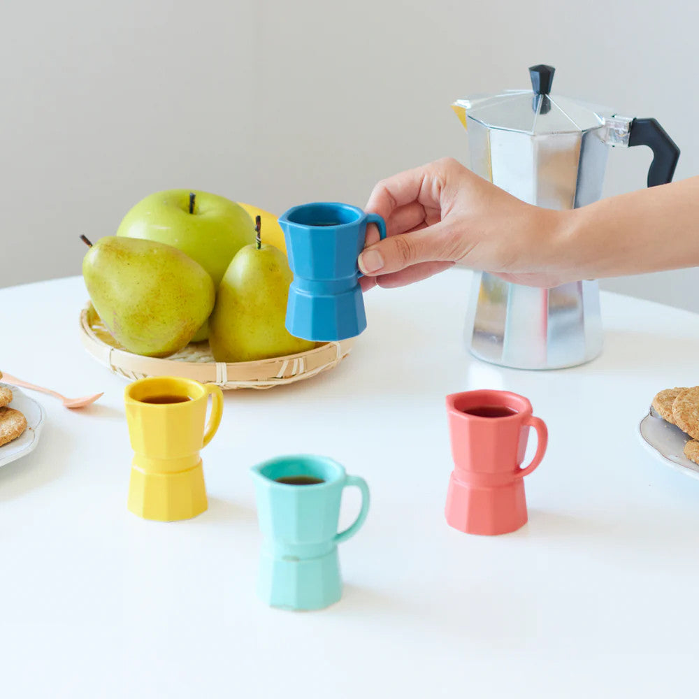 Four ceramic espresso cups with moka pot and coffee being poured