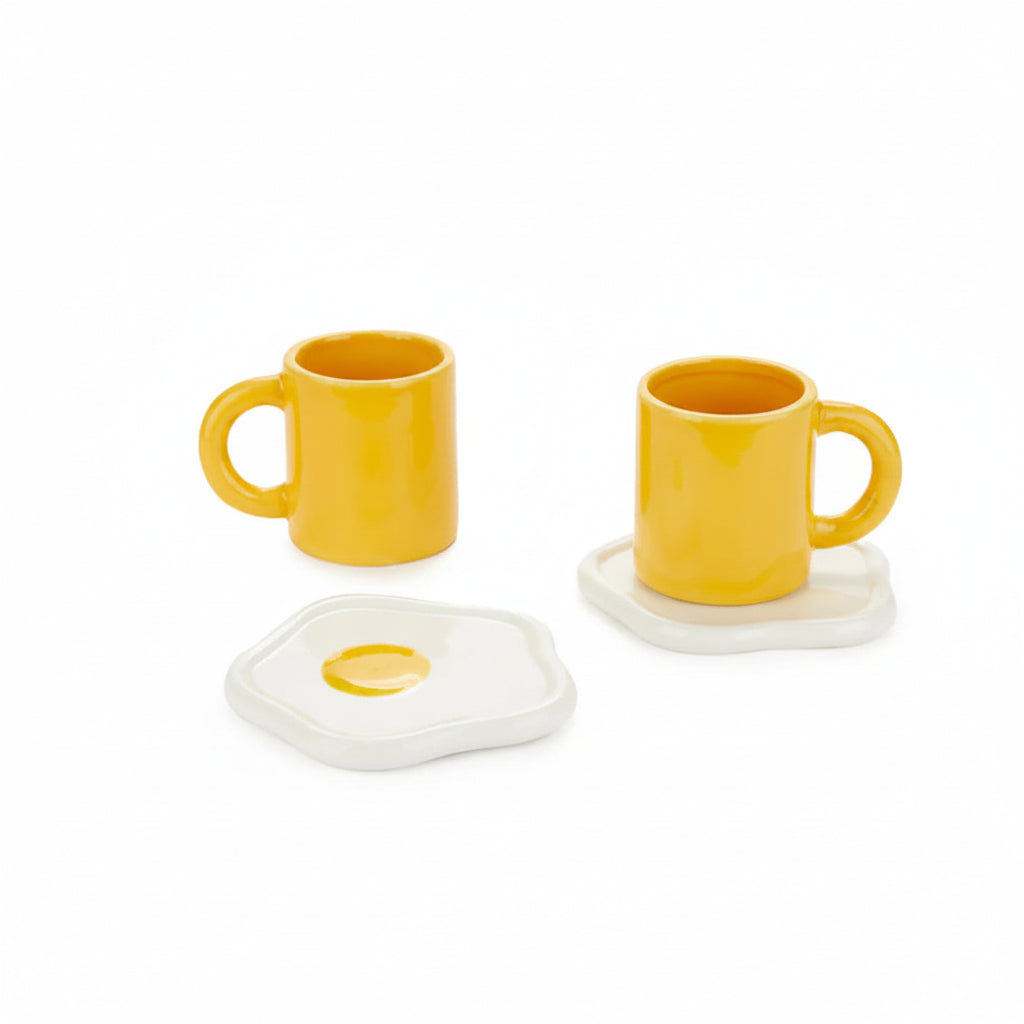 Two yellow cups with fried egg saucers on white background