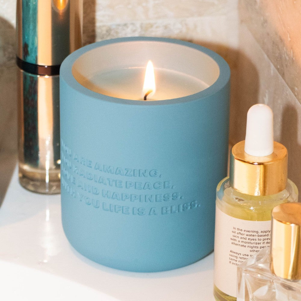 Lit blue cement candle with gold dropper bottle in lifestyle setting
