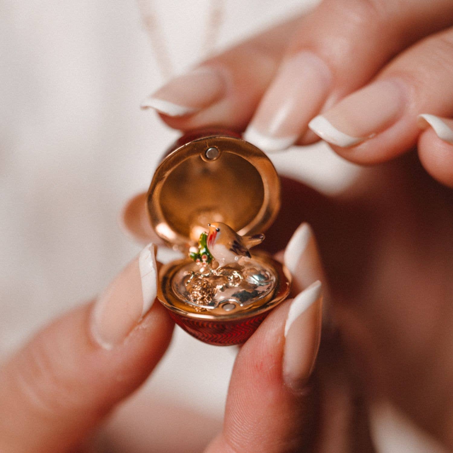 Close-up of open Bill Skinner Robin Egg Locket revealing hand-painted festive robin inside gold enamel interior.