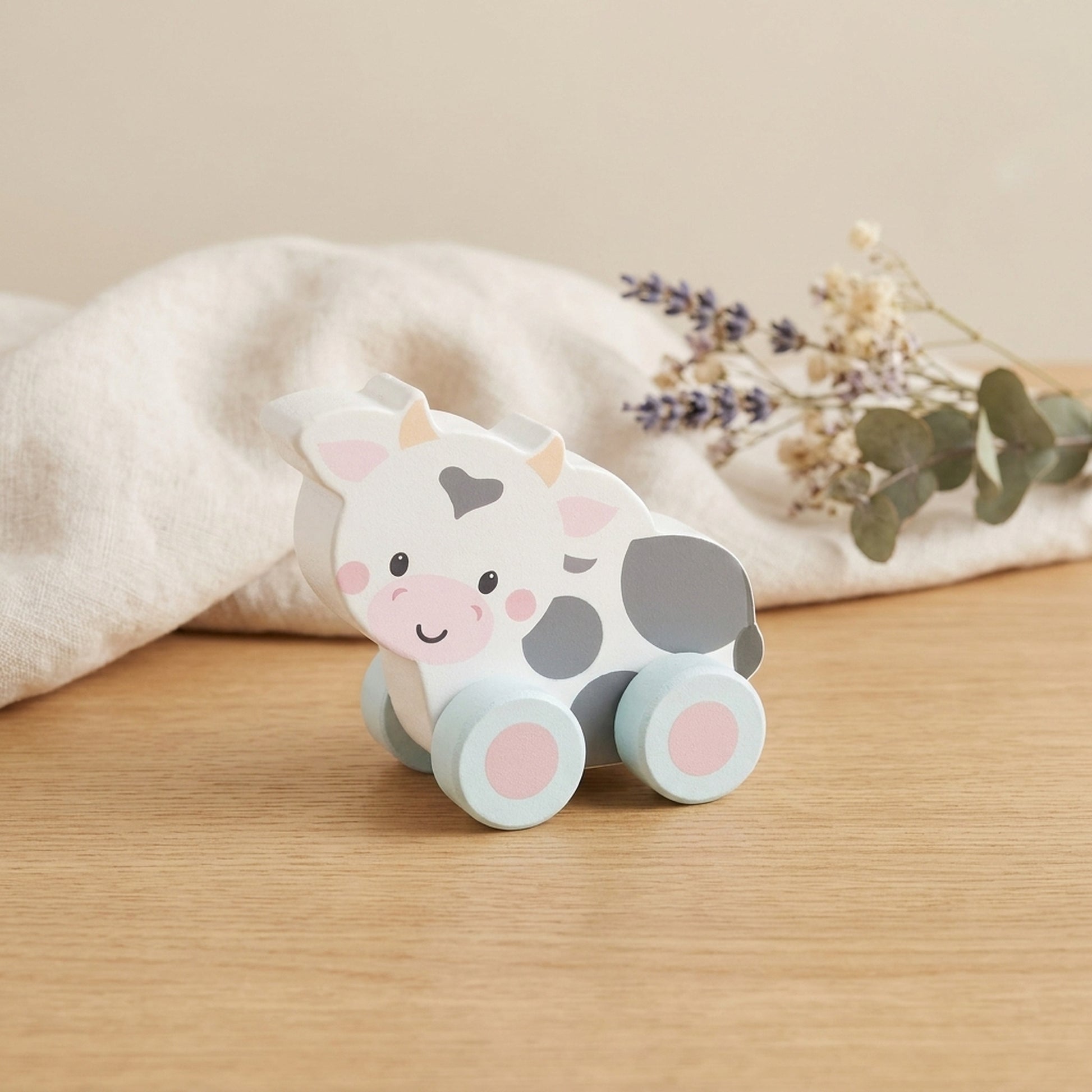 Wooden cow push toy on a warm oak table with cream linen and dried flowers
