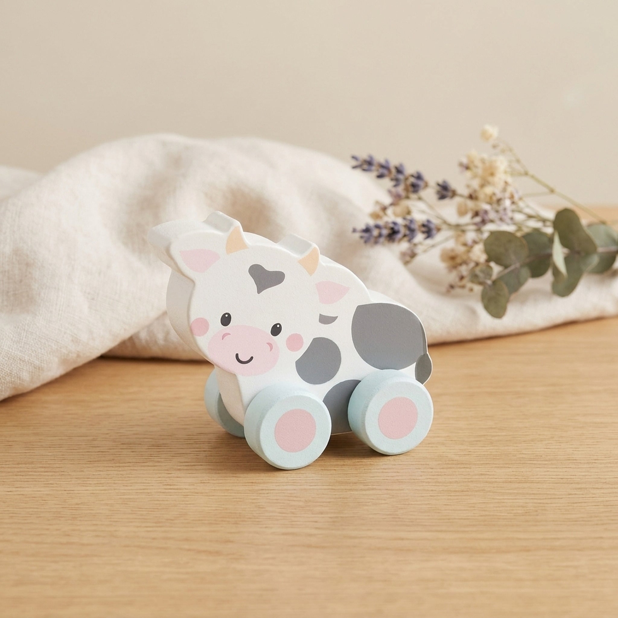 Wooden cow push toy on a warm oak table with cream linen and dried flowers