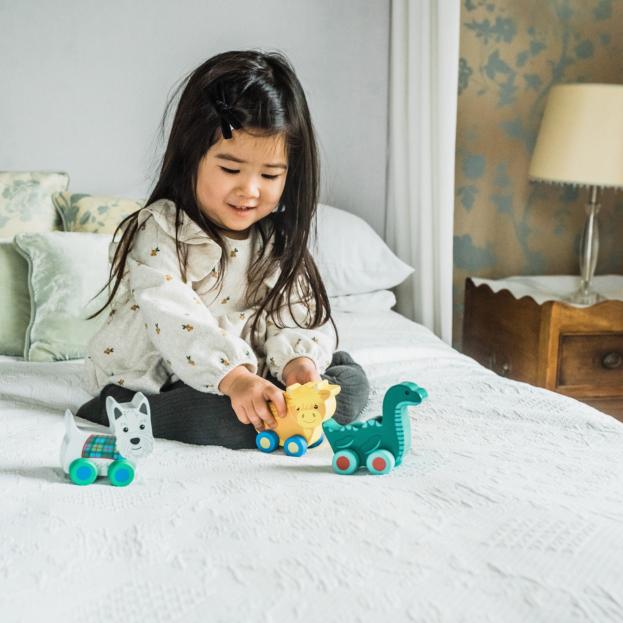 Child on a bed playing with the Scotland range of wooden push toys together
