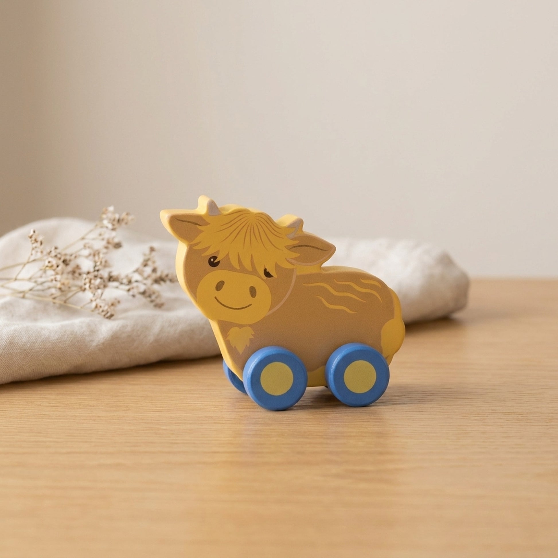 Highland cow wooden push toy on a warm oak table with cream linen and dried flowers