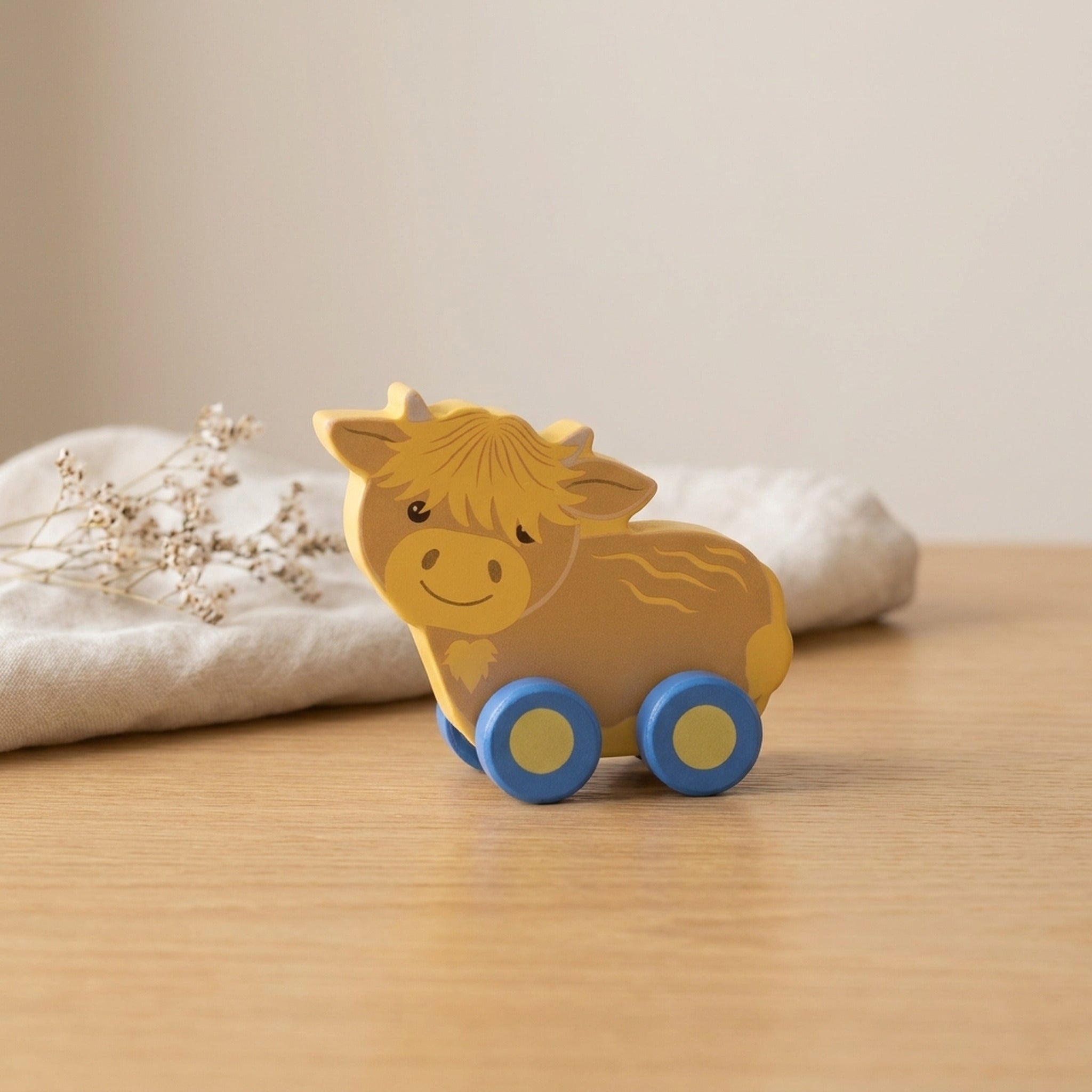 Highland cow wooden push toy on a warm oak table with cream linen and dried flowers