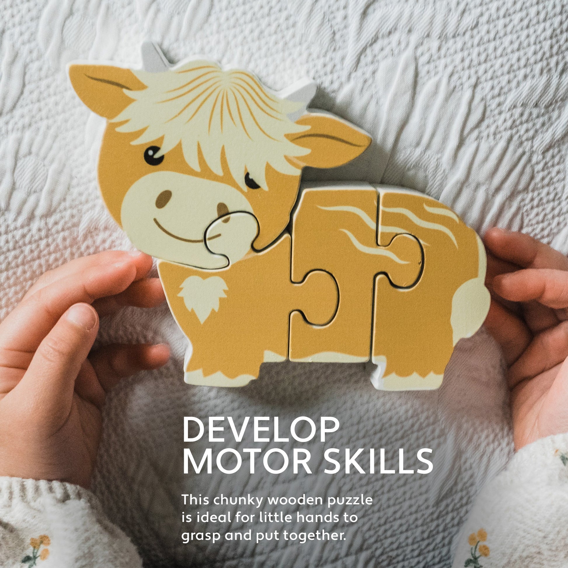 Hands holding the Highland cow wooden puzzle above a cream knitted blanket