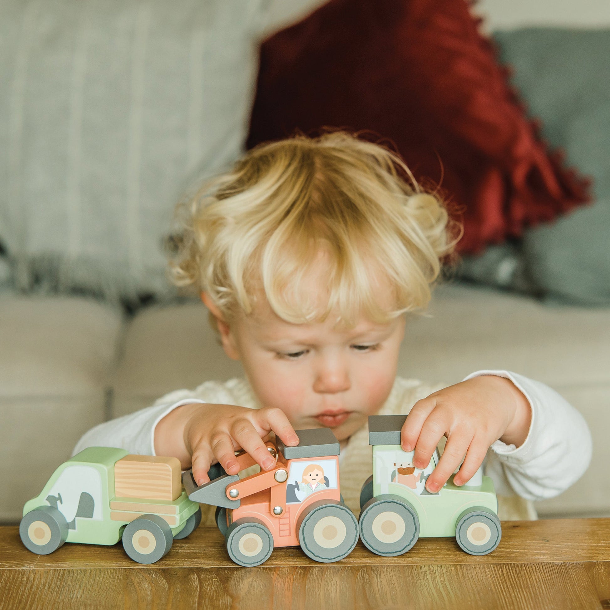 Toddler pushing wooden farm vehicles along a carpet at home