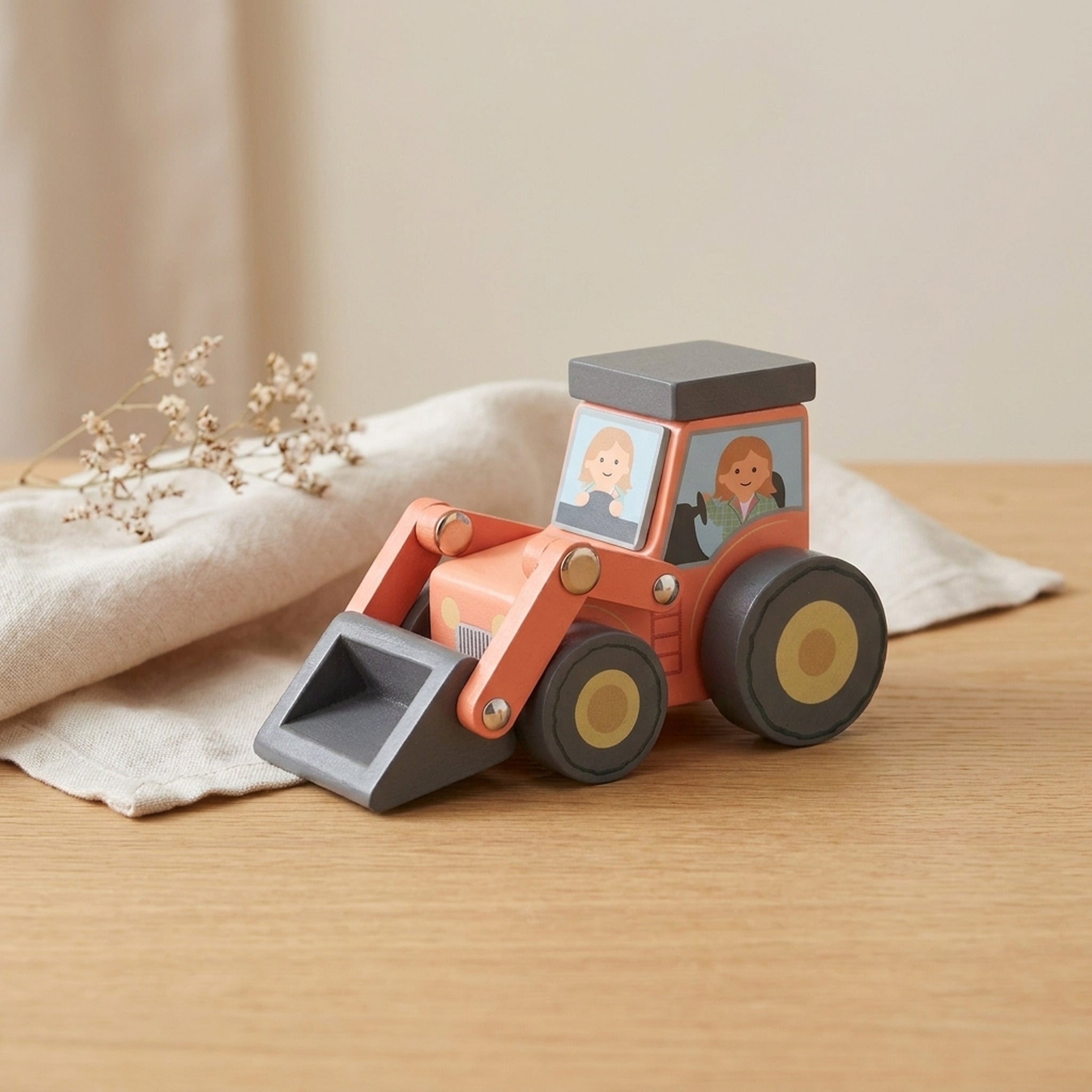 Wooden loader tractor toy on a warm oak table with cream linen and dried flowers
