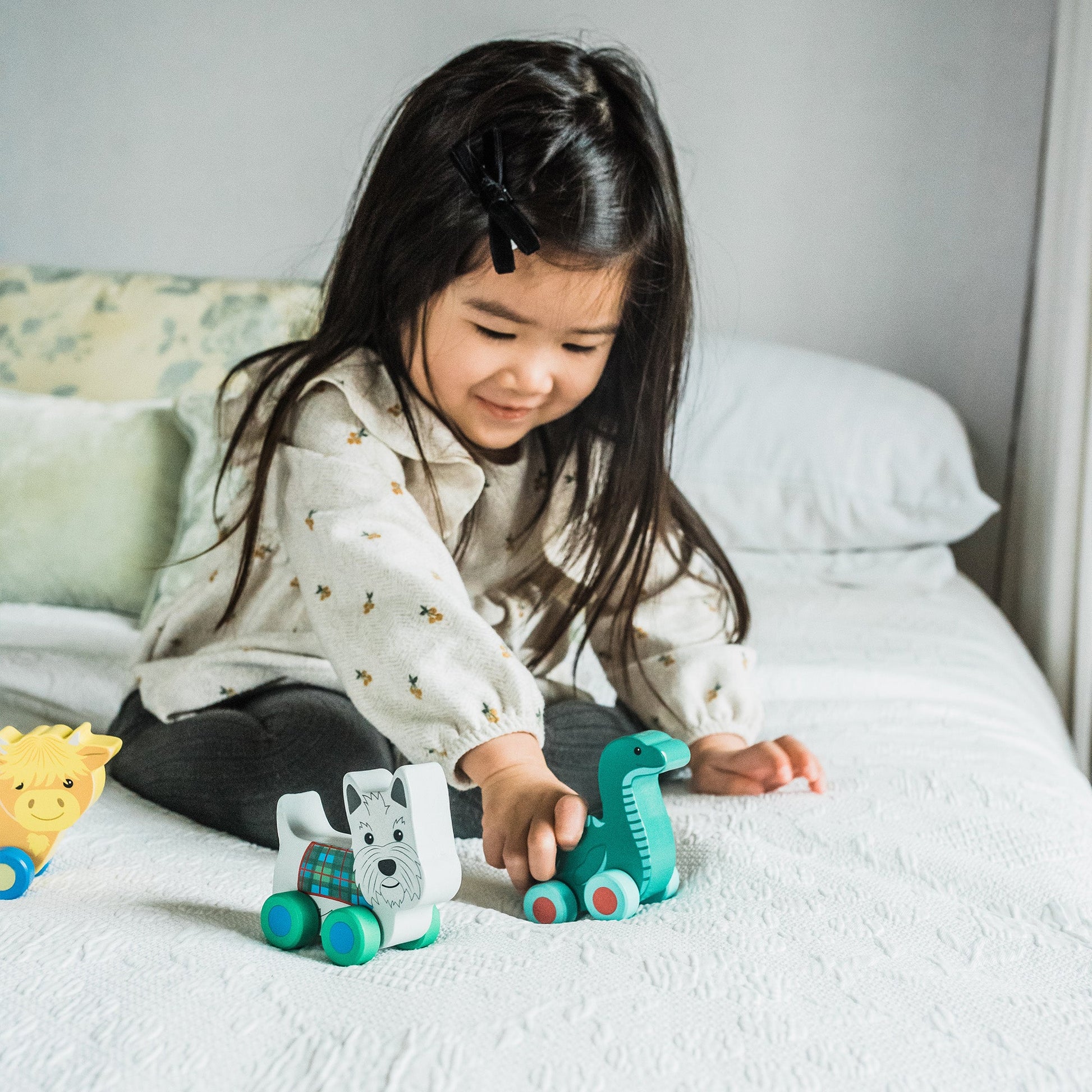 Child on a bed playing with the Scotland range of wooden push toys together