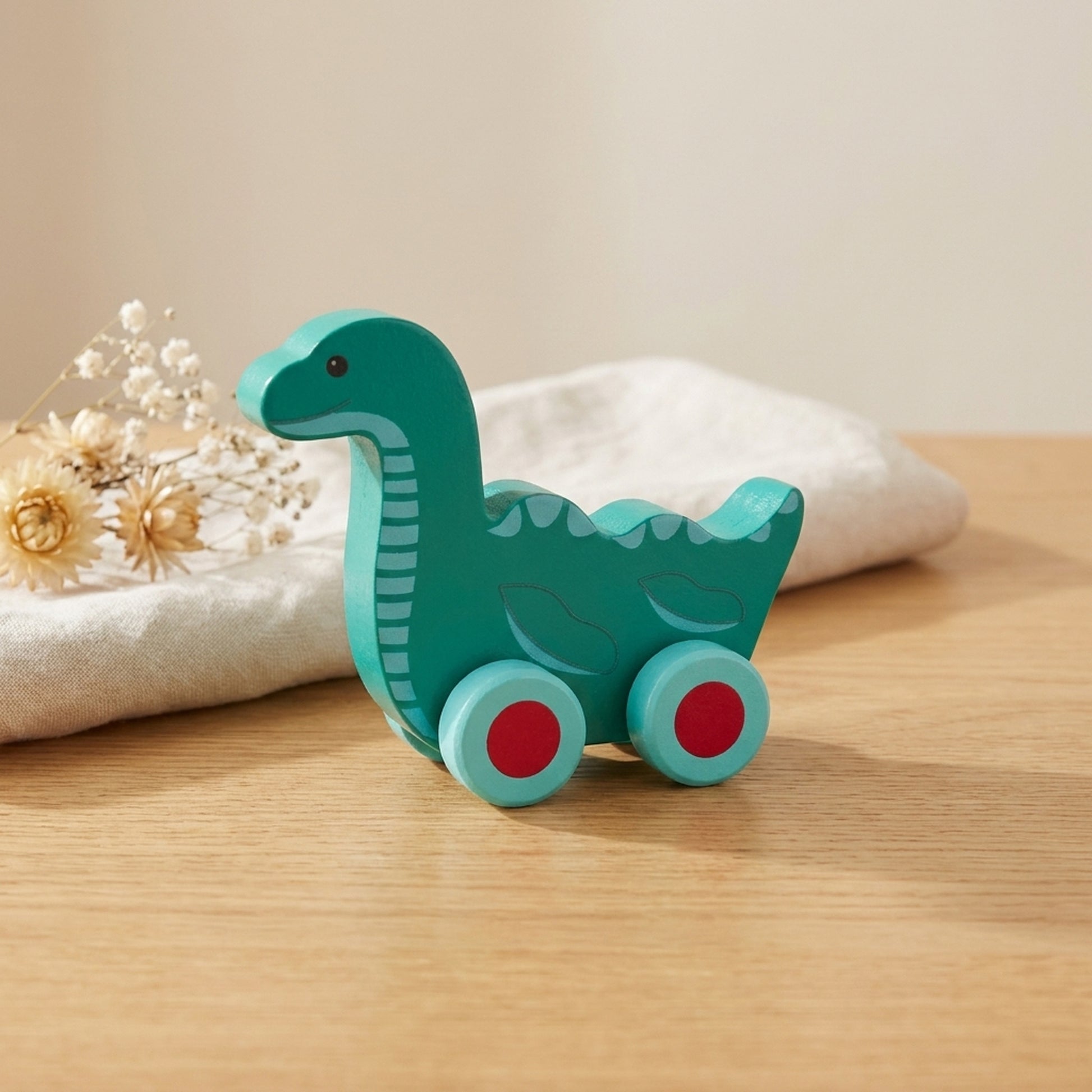 Teal wooden Nessie push toy on a warm oak table with cream linen and dried flowers
