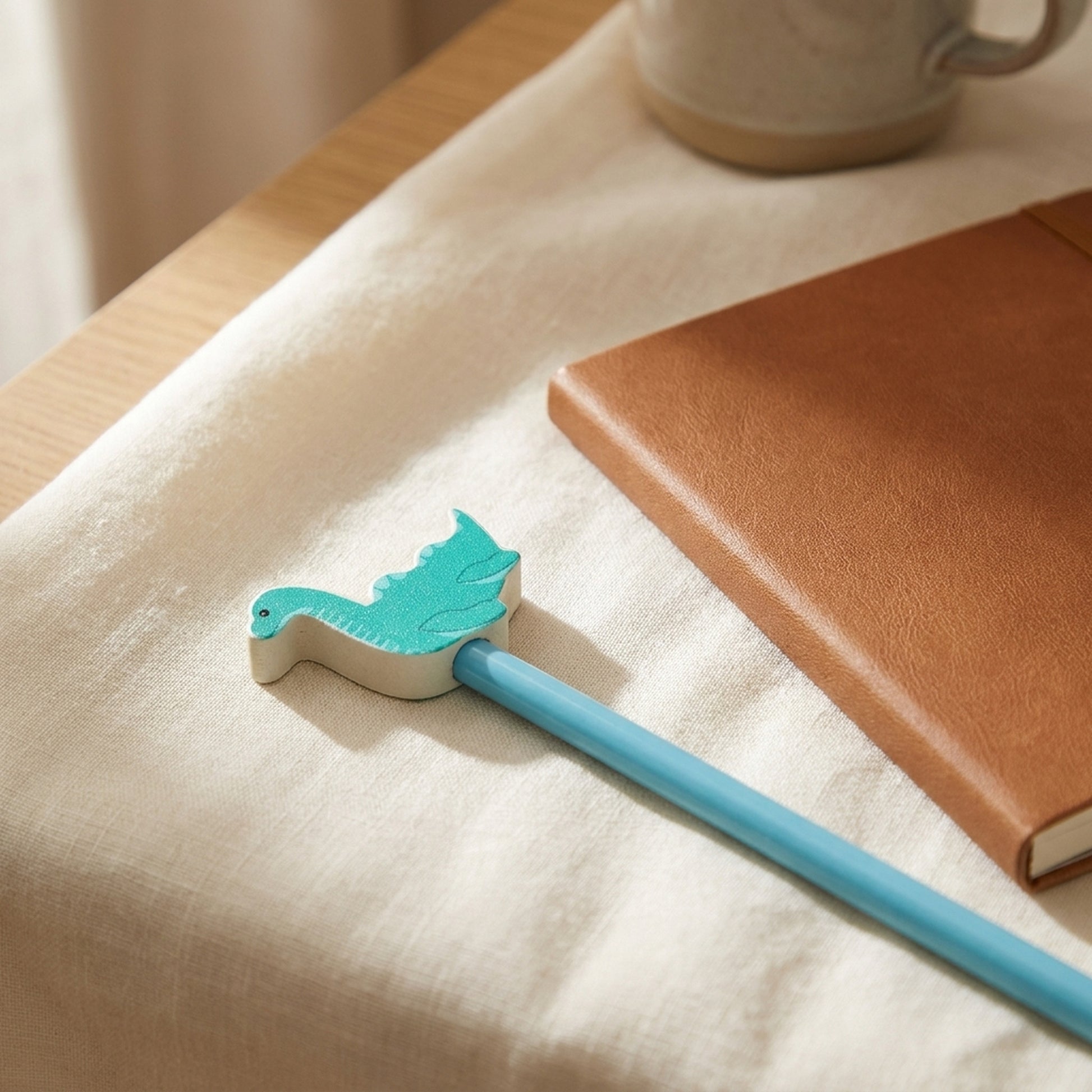 Nessie wooden pencil laid on soft cream linen beside a leather notebook