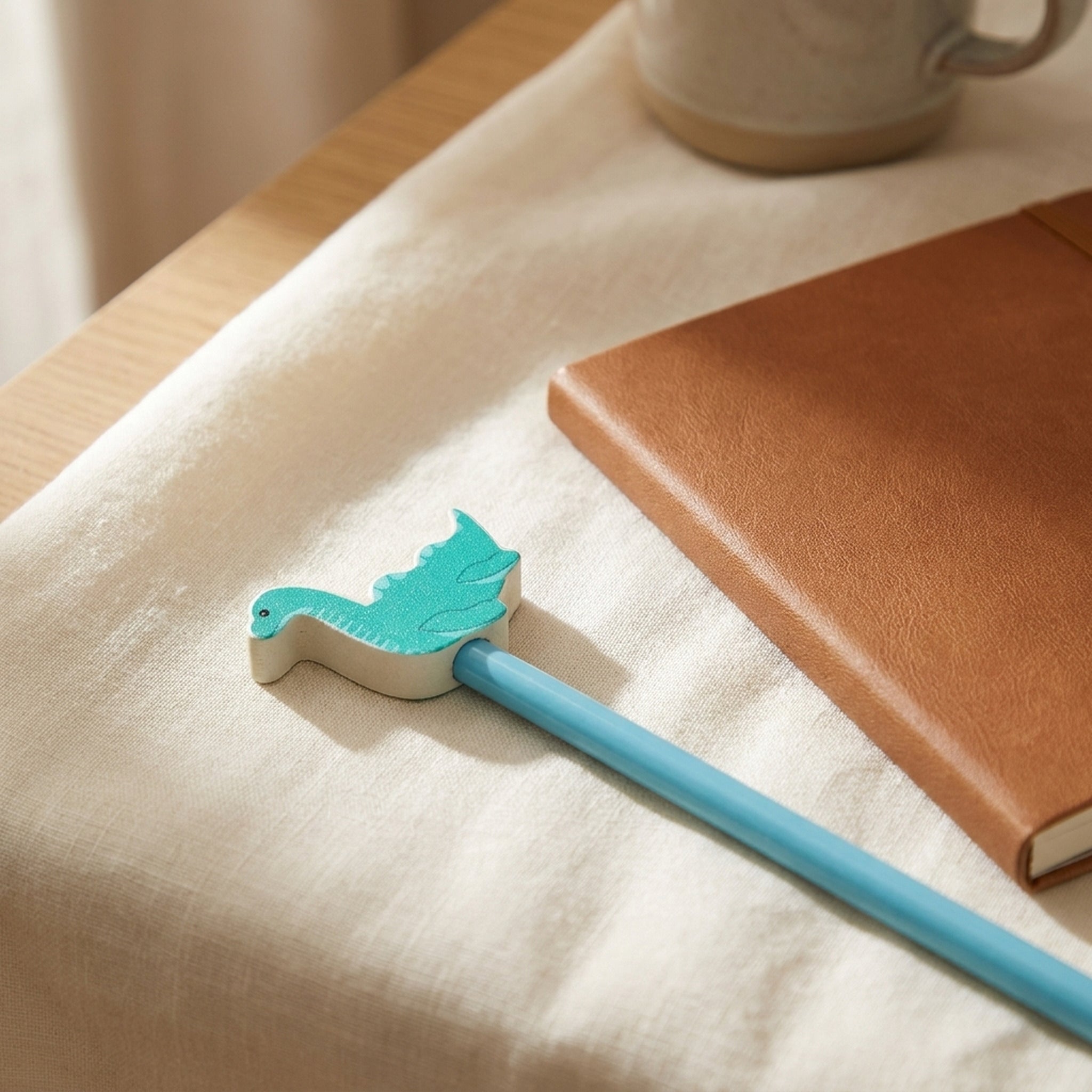 Nessie wooden pencil laid on soft cream linen beside a leather notebook