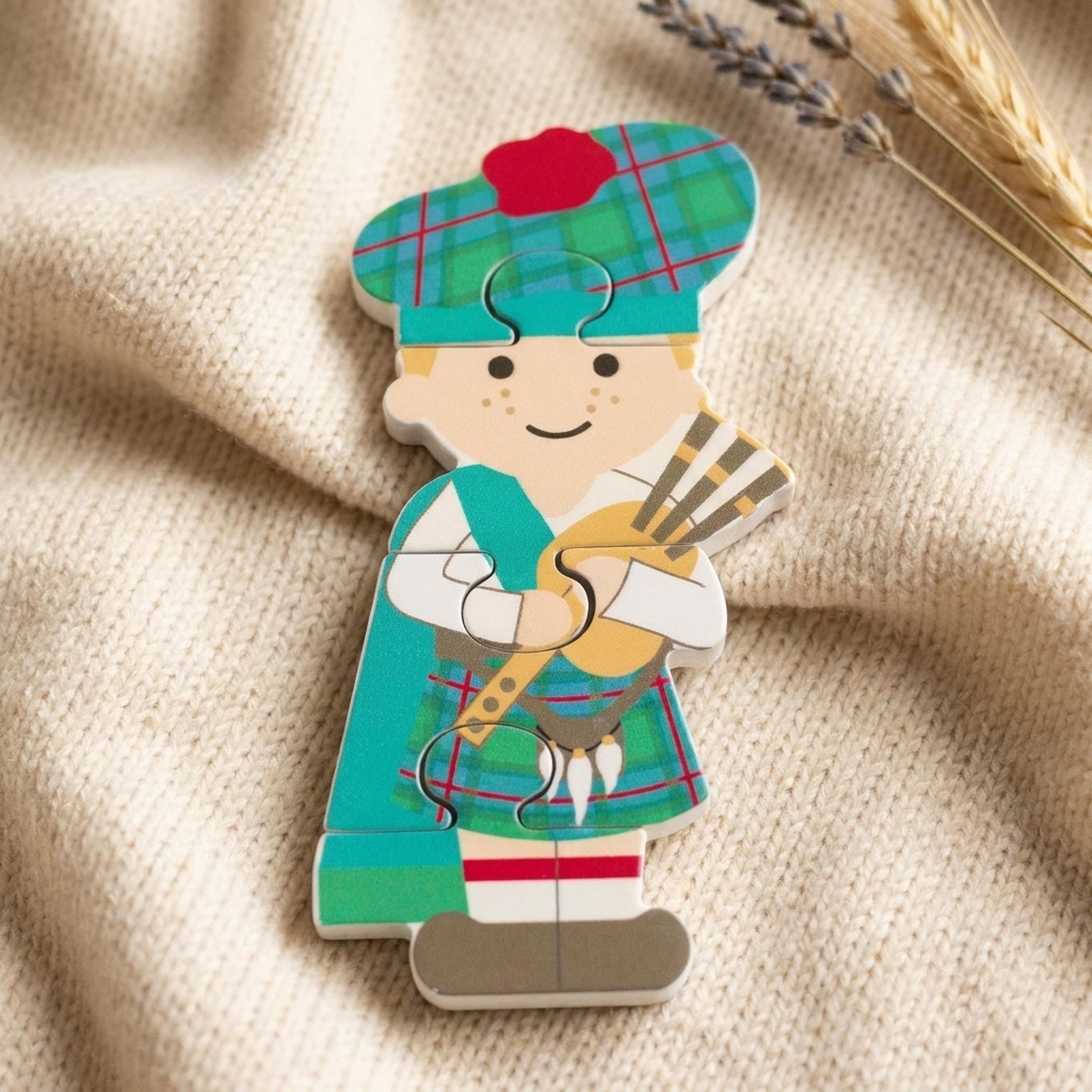 Scottish piper wooden puzzle resting on a soft cream knitted blanket with dried flowers